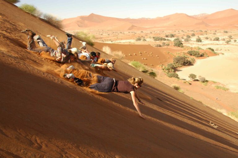Groep toeristen glijdt van de duinen af in de Sossusvlei