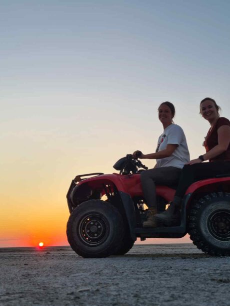 Vrouwen op een quad bij zonsondergang over de Ntwetwe Pan in Botswana