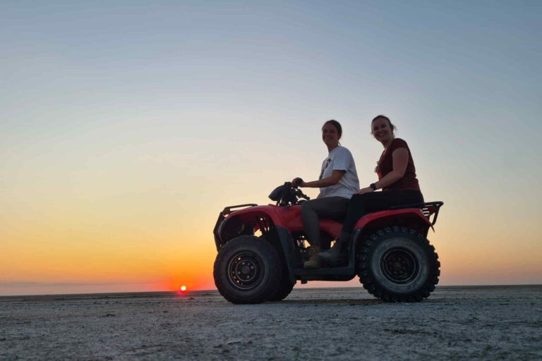 Vrouwen op een quad bij zonsondergang over de Ntwetwe Pan in Botswana