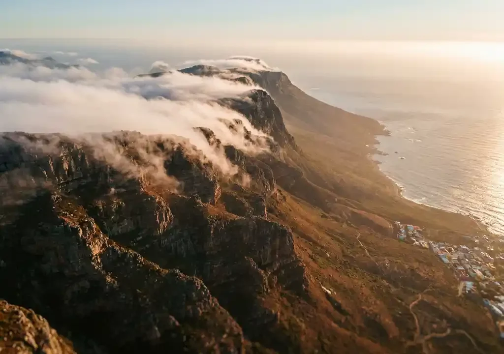 Luchtfoto van de Tafelberg in Kaapstad met wolkentafelkleed, glinsterende Atlantische Oceaan en kleurrijke Bo-Kaap-daken in gouden uurtjelicht.